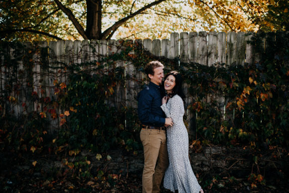 a couple embrace during an engagement session in beautiful light in front of a wood fence with ivy