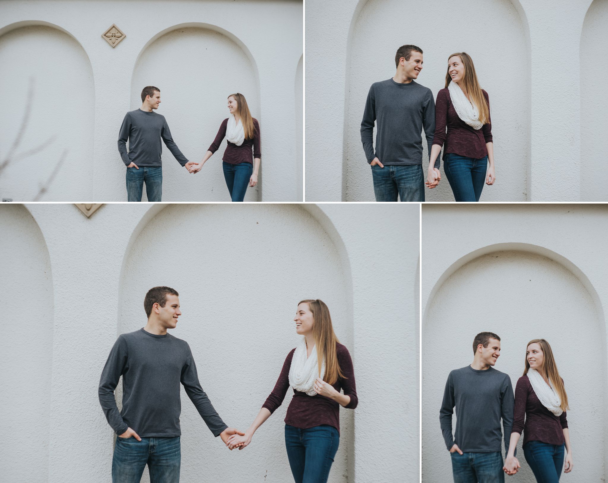 A couple casually stands in front of a white stucco wall, holding hands, at Blackburn Park during their engagement session.  