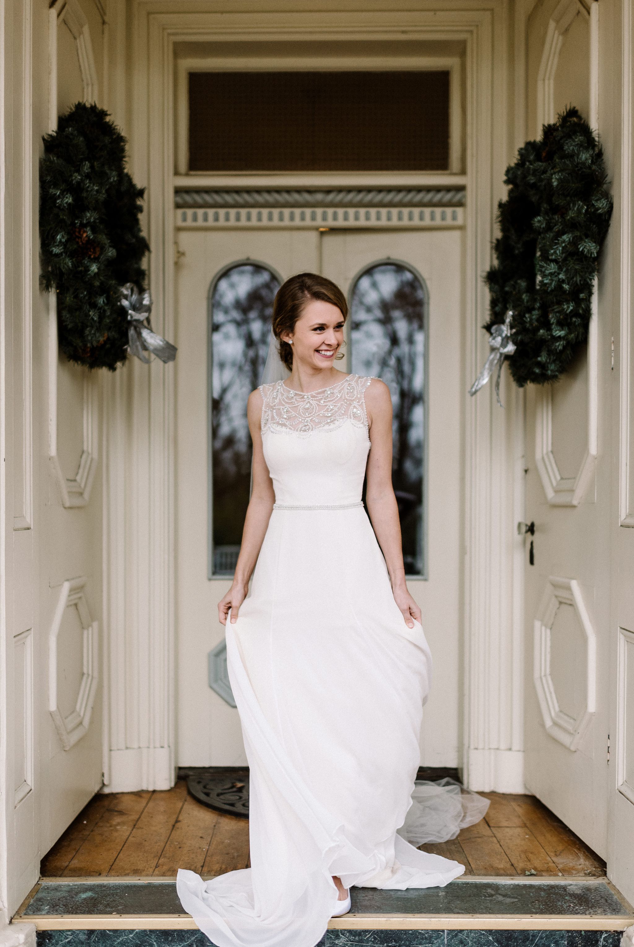 A bride stands on the front porch of the Larimore House. She is smiling.