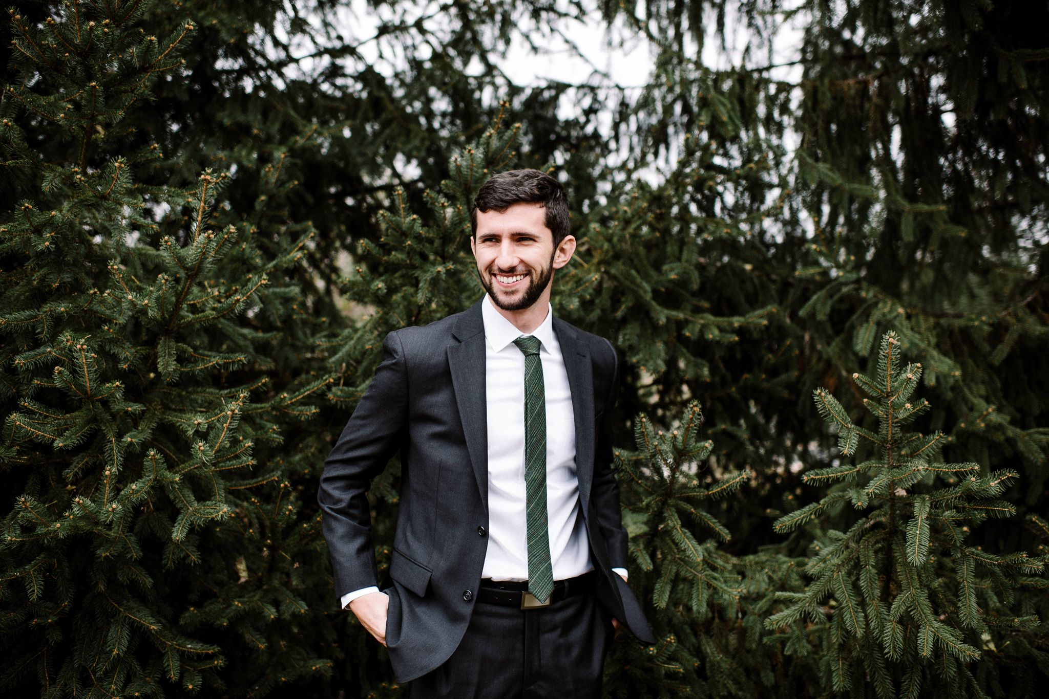 A portrait of a groom in front of pine trees.