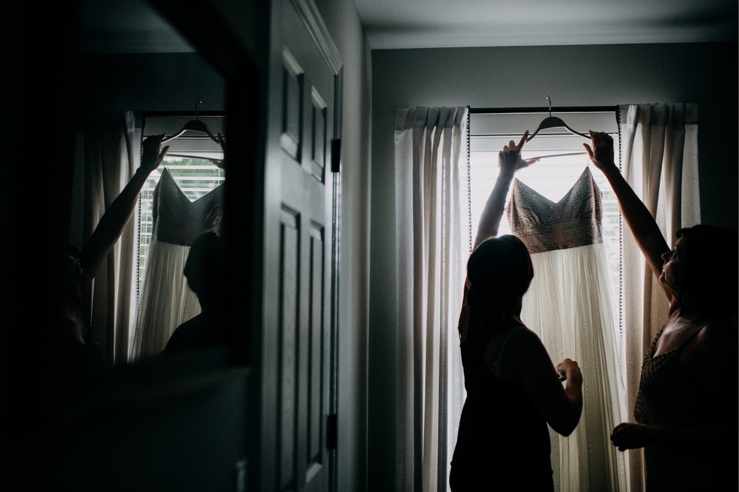 bride reaching for her dress that is hanging from a curtain rod